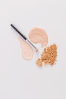 Two samples, liquid spots of foundation, loose dry powder, makeup brush on a white vertical background. top view. A copy space photo