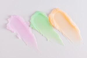 Three multicolored smeared lip balm samples on a white background. Cosmetic texture sample. delicate pastel texture colors. Layout for presentation. photo