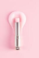 An open package of a tube of lip balm with a delicate structure to moisturize and nourish the lips lies on a sample of rose balm. vertical top view photo