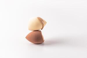 The delicate liquid texture of foundation powder in a natural tone flows down on a blender sponge. Two sponges of different colors. white background. photo