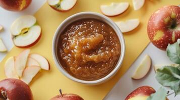 Fresh Homemade Apple Sauce in a Bowl Surrounded by Sliced and Whole Apples on a Yellow Background photo