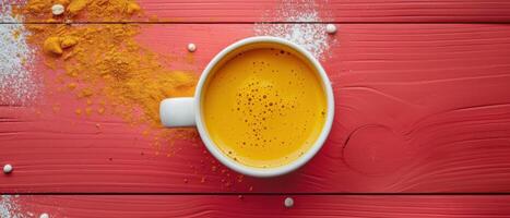 Top View of a Cup of Golden Turmeric Latte on a Vibrant Red Wooden Table with Spices photo