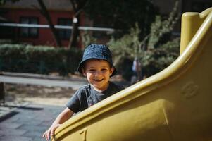 happy kindergarten boy rides a slide on playground in summer photo