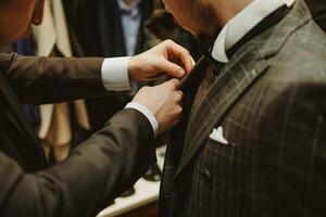 Groom Preparing for Wedding with Best Man Adjusting Suit Jacket in Dressing Room photo