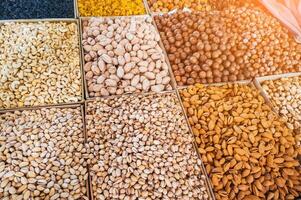 assortment of different variety nuts and dried fruits on counter at oriental bazaar. Almonds, raisins, pistachios, hazelnuts, macadamia in market stall photo