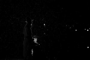dark silhouette of a man in a hat at night in the rain in the city photo