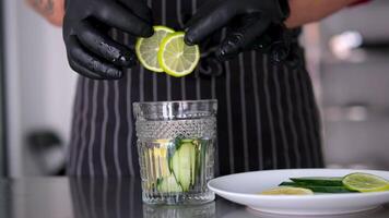 Add lemon to glass. Making lemonade, summer drink, cold drink, healthy liquid. Throw a slice of lemon into a glass Citrus fall water dropped glass closeup. Cold water with ice cubes and lemon slice video