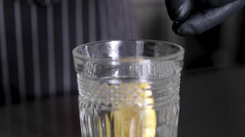 Close of lemon slice in female hand dropping in water and ice cubes in blue glass. Round lemon piece in beverage in slow motion macro view. video