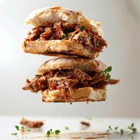 A close up of a pork belly sandwich with bacon, barbecue sauce and garnishes on top. photo