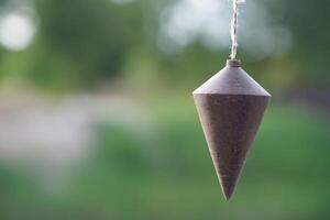Old plumb bob, plummet or conical iron hanging with rope for measurement level, use for determining perpendicularity . Concept, work tool for construction and carpentry. photo