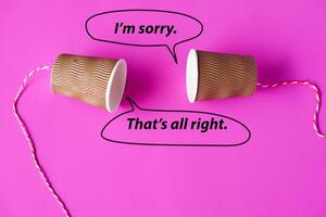 Paper cups with string on pink background with words. Hello, I'm sorry. That's all right. Concept, English conversation. Teaching aid. Cummunication. DIY telephone toy. photo