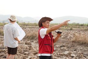 Asian father and son are exploring and surveying their own land, father holds binocular and points to boundary, son holds map. Concept, land property, legacy.Exploration. photo