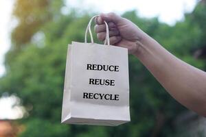 Hand hold brown paper bag with text Reduce Reuse Recycle. Concept, eco friendly packaging for containing things, can use many times. Reduce, Reuse, Recycle for conserve environment. Reduce plastic bag photo