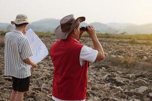 Asian father and son are exploring and surveying their own land, father holds binocular and points to boundary, son holds map. Concept, land property, legacy.Exploration. photo