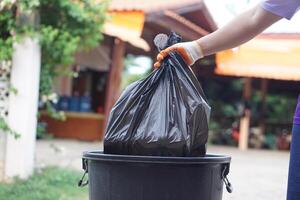 Hand holding garbage black bag putting in to the bin. Concept, garbage management, Keep clean for sanitary and community service for the best environment. Zero waste. photo
