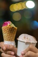 Close up hand of a person holding a cup and a cone of ice cream with blurred background photo
