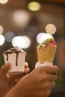 Close up hand of a person holding a cup and a cone of ice cream with blurred background photo