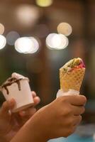 Close up hand of a person holding a cup and a cone of ice cream with blurred background photo