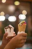 Close up hand of a person holding a cup and a cone of ice cream with blurred background photo