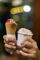Close up hand of a person holding a cup and a cone of ice cream with blurred background photo