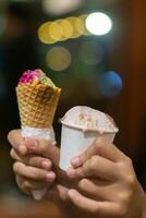 Close up hand of a person holding a cup and a cone of ice cream with blurred background photo