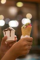Close up hand of a person holding a cup and a cone of ice cream with blurred background photo