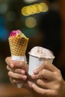 Close up hand of a person holding a cup and a cone of ice cream with blurred background photo