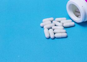 Pills spilled out of white bottle on blue background. Mock up for special offers as advertising or other ideas. Medical, pharmacy and healthcare concept. Copy space. Empty place for text or logo photo