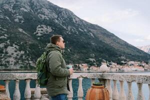 Man with a thermal mug stands near a balustrade and looks into the distance. Side view photo
