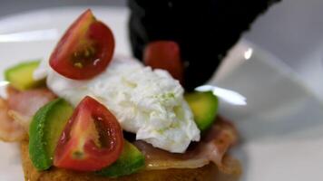 Poached egg Benedict on a sandwich plate hollandaise sauce cutting with fork and knife in outdoor restaurant. Classic breakfast meal with poached eggs, bacon on English muffin. Delicious video