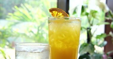 Rainbow paradise cocktail with a orange slice and a straw on a rustic white washed table on a tropical beach. Turquoise sea in the background video