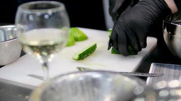 Slice cucumber cook cuts a spring salad of tomatoes, cucumbers, greens and mixes. Woman cutting cucumber for salad on wooden cutting board on kitchen table with cucumbers, tomatoes branch video