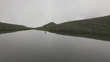 Woman tourist hike in mountain by pristine alpine lake in foggy weather outdoors video