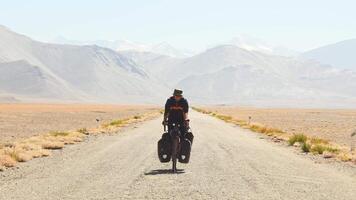 Front view adventurous caucasian male traveller cycle bicycle touring solo on asphalt famous Pamir highway M41 road in remote high Pamir mountains. Pamir highway adventure travel route destination video