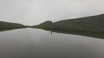 Woman tourist hike in mountain by pristine alpine lake in foggy weather outdoors video