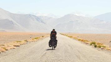 Front view adventurous caucasian male traveller cycle bicycle touring solo on asphalt famous Pamir highway M41 road in remote high Pamir mountains. Pamir highway adventure travel route destination video