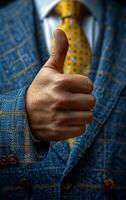 A man in a suit is giving a thumbs up. The man is wearing a blue jacket and a yellow tie photo