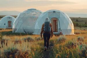 A man carrying a backpack is walking in the direction of a dome tent photo