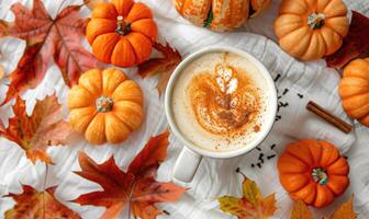 A warm pumpkin chai latte, topped with a sprinkle of cinnamon surrounded by small pumpkins and vibrant autumn leaves photo