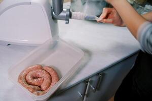 Cook corrects the intestine on the nozzle of the electric meat grinder next to the sausages in the box photo
