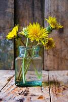 Small bouquet of dandelions in a glass vase on a wooden background. Minimalism. photo