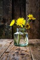 Small bouquet of dandelions in a glass vase on a wooden background. Minimalism. photo