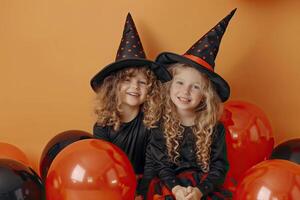 Two little girls in black witch costumes on orange background with balloons. photo