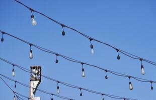 Lamp bulbs on wire string isolated on horizontal outdoor bright blue sky background. photo