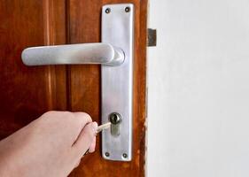 Hand holding key to unlock door knob isolated on horizontal brown door background. photo