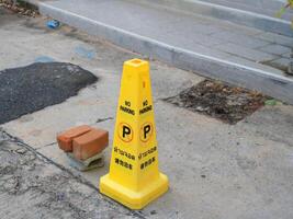 Yellow plastic traffic cone on street in Thailand and no parking letters in tree language Thai English and Japanese photo