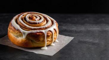 Cinnamon roll with white glaze on black background, selective focus photo