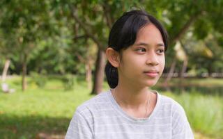 Portrait Asian pretty female teenager in casual dress looking at the view while standing in the park. People lifestyle. Generation z. Simple living. photo
