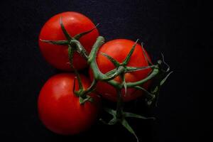 Three vibrant tomatoes on the vine set against a dark background, showcasing their rich red color and glossy texture in a striking, minimalist composition. photo