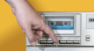 man's hand crushing the key of old aluminum recorder with music cassette inside against yellow background photo
